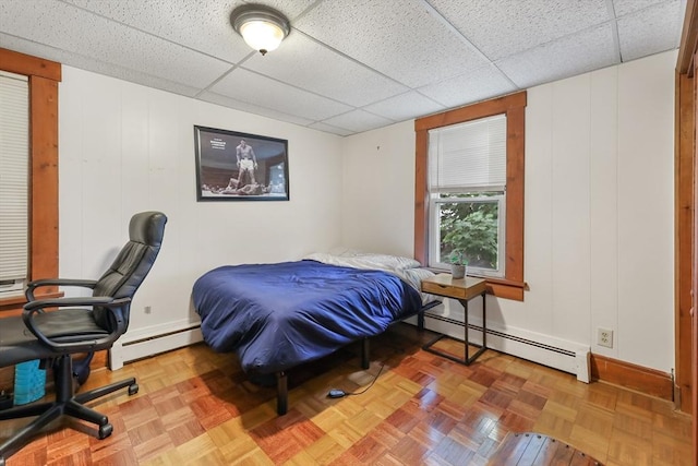 bedroom with a baseboard heating unit, parquet floors, and a paneled ceiling