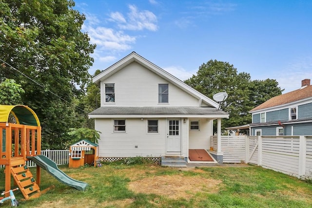 rear view of property with a playground and a lawn