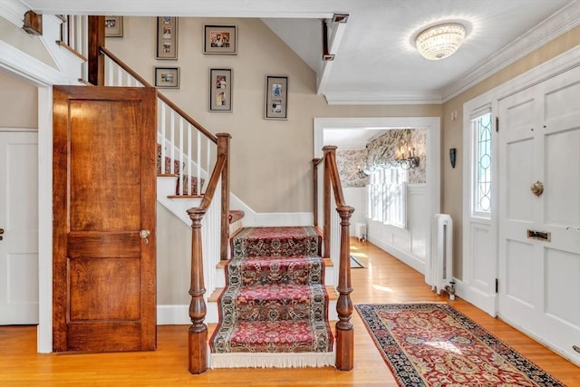 foyer entrance featuring stairs, wood finished floors, radiator heating unit, and ornamental molding