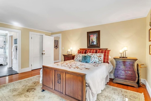 bedroom with baseboards, ensuite bath, light wood-style flooring, and ornamental molding