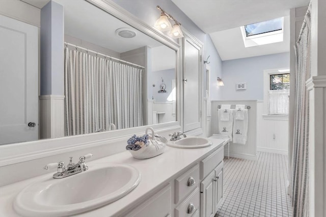 full bathroom featuring tile patterned flooring, a wainscoted wall, a skylight, and a sink