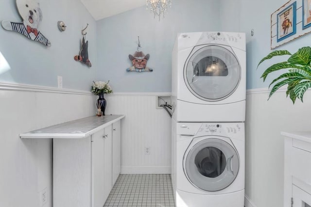 laundry room with stacked washer / dryer, light tile patterned flooring, cabinet space, and wainscoting