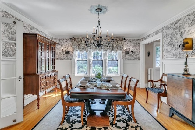 dining room featuring a wainscoted wall, light wood-style floors, ornamental molding, and wallpapered walls