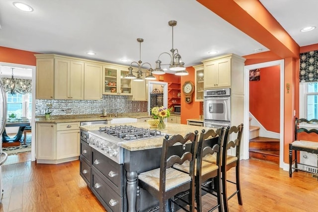 kitchen featuring light wood finished floors, glass insert cabinets, a chandelier, appliances with stainless steel finishes, and cream cabinetry