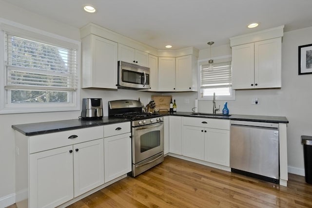 kitchen featuring sink, light hardwood / wood-style flooring, appliances with stainless steel finishes, white cabinetry, and hanging light fixtures