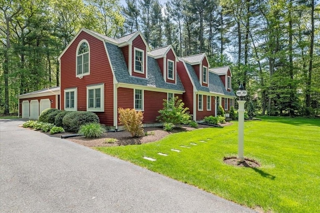 view of front facade featuring a gambrel roof, a shingled roof, driveway, a front yard, and an attached garage