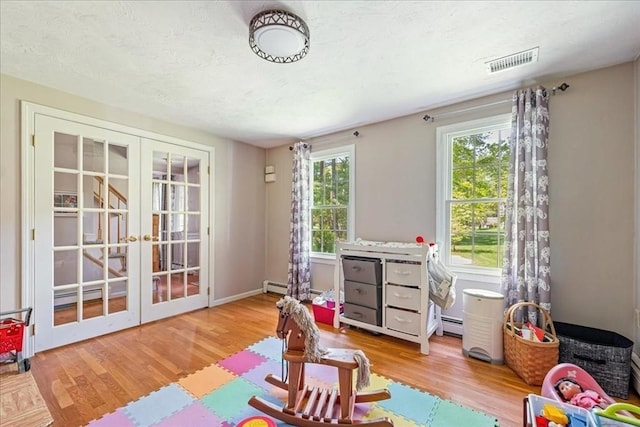 rec room featuring french doors, light wood-style floors, a textured ceiling, and baseboard heating