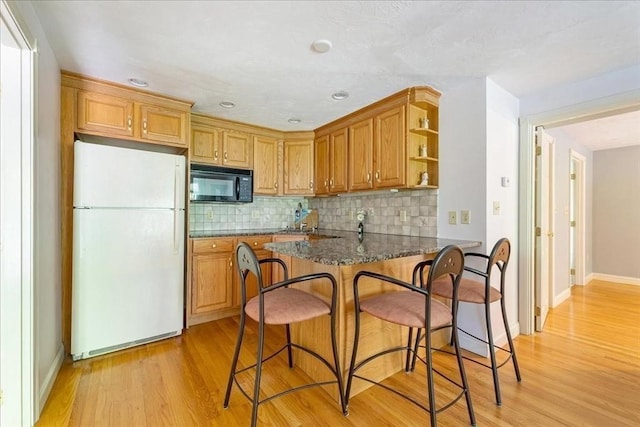 kitchen featuring freestanding refrigerator, black microwave, light wood-style floors, tasteful backsplash, and recessed lighting