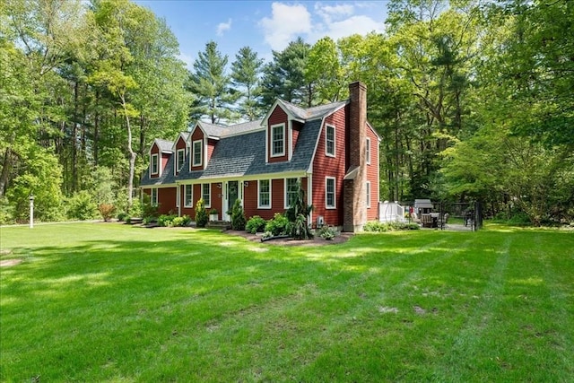 dutch colonial featuring a gambrel roof, a front yard, and a chimney