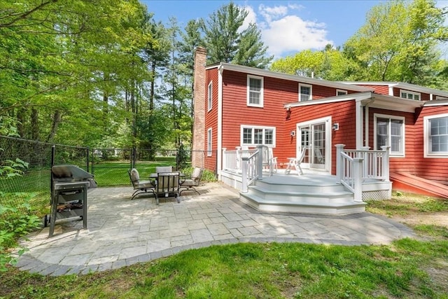 rear view of house featuring a chimney, a patio, fence, a deck, and view of wooded area