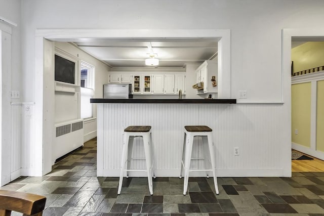 453 Washington St, Gloucester, MA 01930 - kitchen with radiator, freestanding refrigerator, dark countertops, a peninsula, and white cabinetry