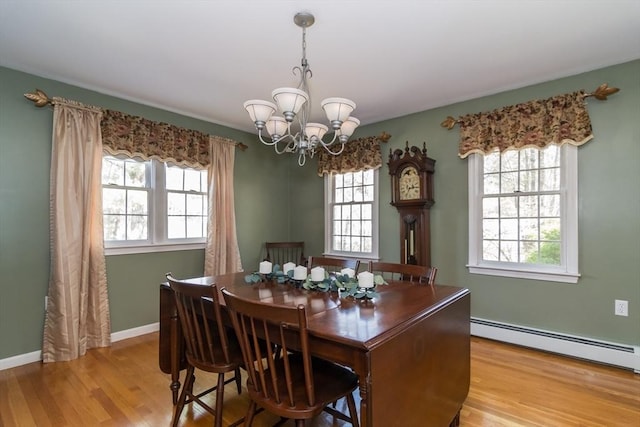 dining space featuring a healthy amount of sunlight, baseboard heating, light wood finished floors, and a notable chandelier