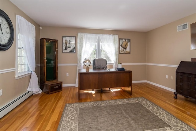 home office featuring a baseboard heating unit, a healthy amount of sunlight, wood finished floors, and visible vents