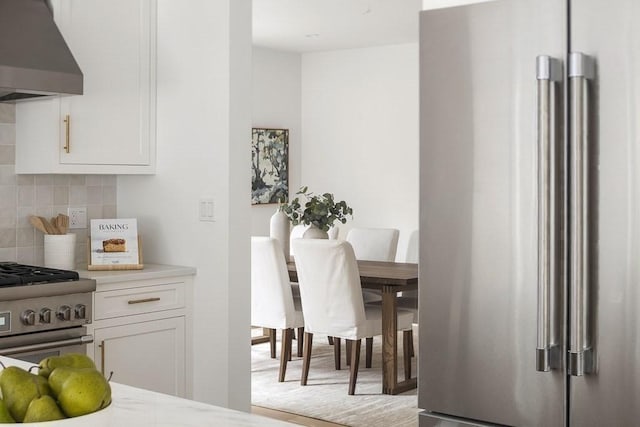 kitchen with backsplash, premium appliances, white cabinets, and ventilation hood