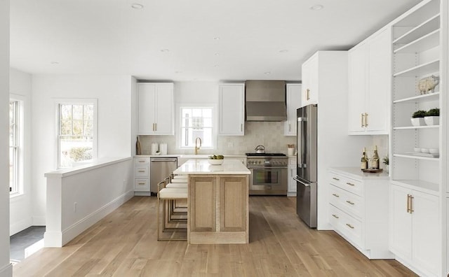 kitchen featuring white cabinets, a center island, wall chimney range hood, high end appliances, and a breakfast bar