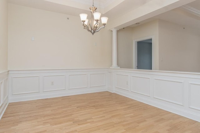 spare room featuring ornate columns, ornamental molding, an inviting chandelier, and light wood-type flooring