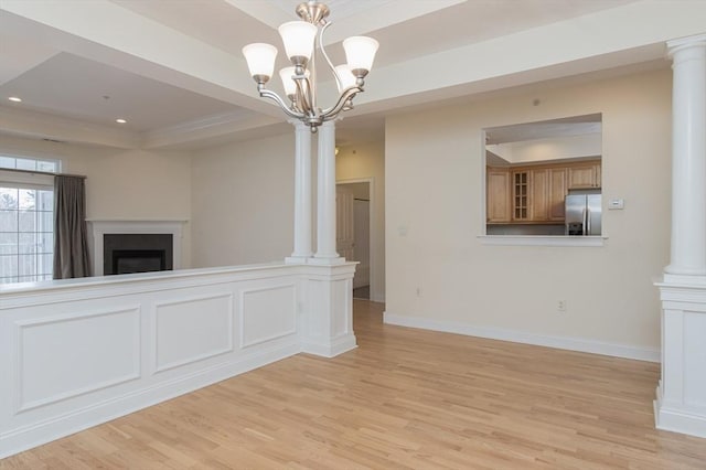 unfurnished living room featuring a tray ceiling, light hardwood / wood-style flooring, and ornate columns