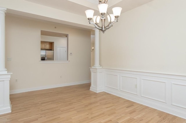 unfurnished dining area featuring ornate columns, an inviting chandelier, and light hardwood / wood-style flooring