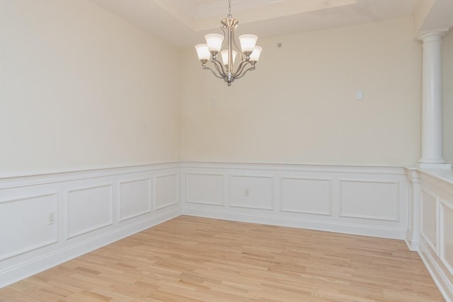 spare room with a notable chandelier, a tray ceiling, light hardwood / wood-style flooring, and decorative columns