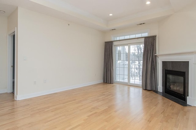 unfurnished living room with a tray ceiling, ornamental molding, a premium fireplace, and light wood-type flooring