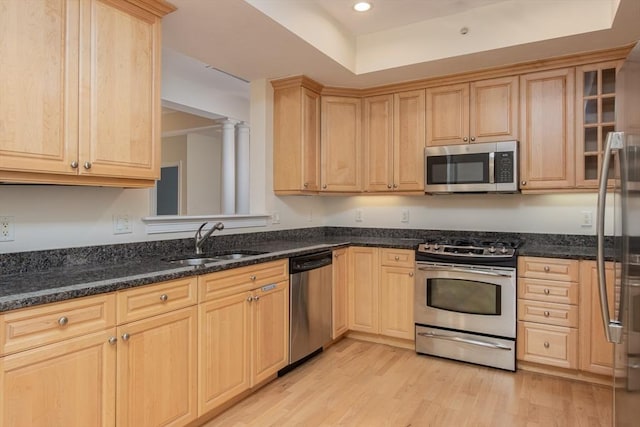 kitchen featuring stainless steel appliances, light hardwood / wood-style floors, sink, and dark stone counters