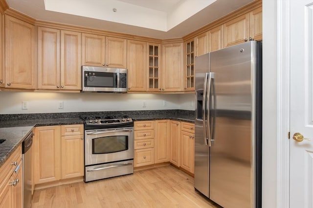 kitchen featuring appliances with stainless steel finishes, light hardwood / wood-style flooring, light brown cabinetry, and dark stone counters