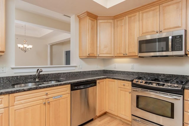 kitchen with sink, stainless steel appliances, a tray ceiling, light brown cabinetry, and dark stone counters