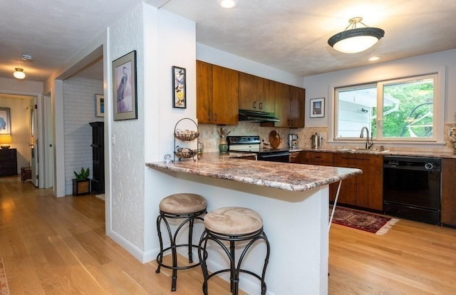 kitchen featuring brown cabinetry, electric range oven, under cabinet range hood, light wood-style floors, and black dishwasher