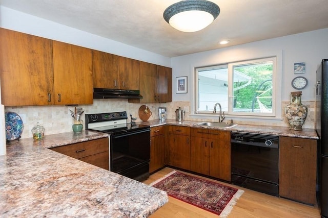 kitchen featuring a sink, light wood-style floors, brown cabinetry, under cabinet range hood, and black appliances