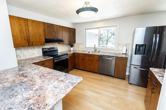 kitchen with a sink, light wood finished floors, stainless steel appliances, backsplash, and under cabinet range hood