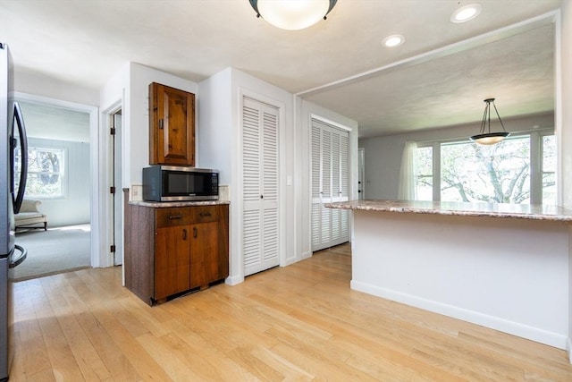kitchen featuring light wood-style floors, baseboards, stainless steel microwave, and brown cabinets