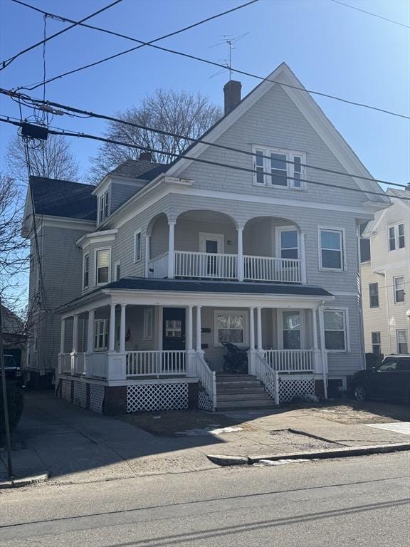 view of front facade featuring a balcony, covered porch, and a chimney