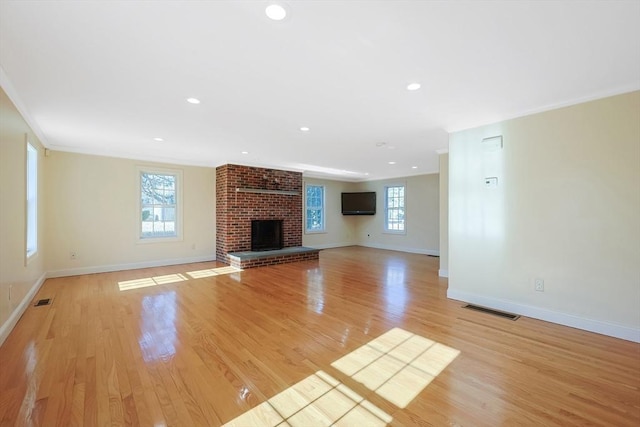 unfurnished living room featuring a brick fireplace, a healthy amount of sunlight, and light hardwood / wood-style flooring