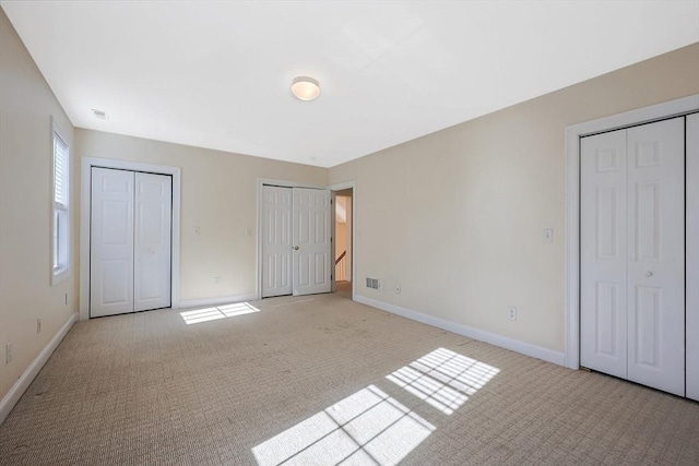 unfurnished bedroom featuring two closets and light colored carpet