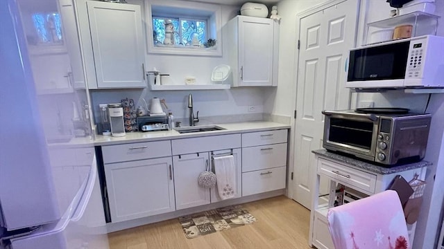 kitchen with a sink, white microwave, light wood-style flooring, and white cabinetry