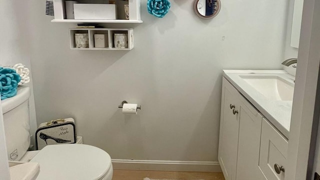 half bathroom with vanity, toilet, wood finished floors, and baseboards