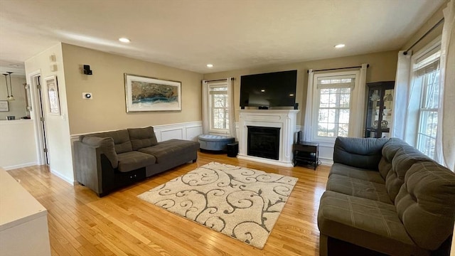 living area with a wainscoted wall, recessed lighting, a fireplace, and light wood-style floors