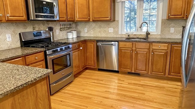 kitchen with dark stone counters, light wood-type flooring, brown cabinets, appliances with stainless steel finishes, and a sink