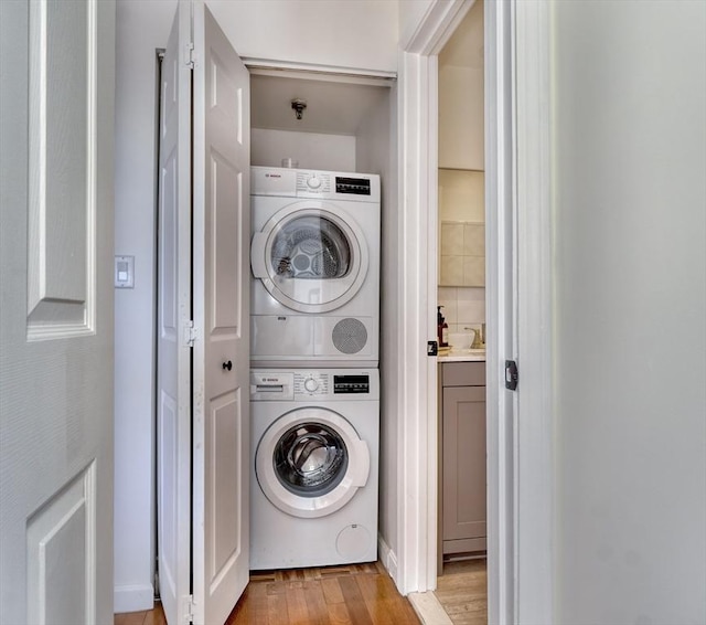 clothes washing area with light wood-type flooring, laundry area, and stacked washing maching and dryer