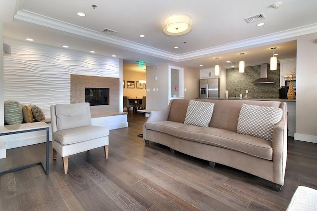 living room featuring recessed lighting, a raised ceiling, visible vents, ornamental molding, and wood finished floors