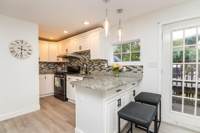 kitchen featuring decorative light fixtures, decorative backsplash, kitchen peninsula, gas range, and light stone countertops