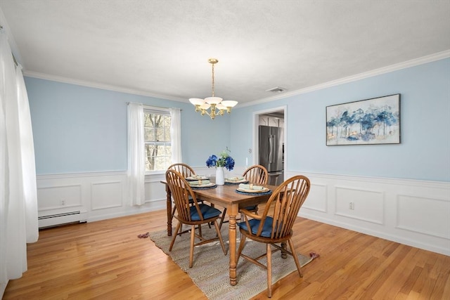 dining room with a baseboard heating unit, crown molding, a chandelier, and light wood-type flooring