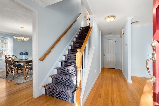 stairs featuring crown molding, hardwood / wood-style floors, and a notable chandelier