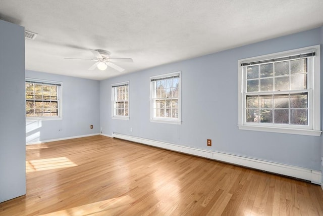 empty room featuring ceiling fan, a wealth of natural light, light hardwood / wood-style flooring, and a baseboard heating unit