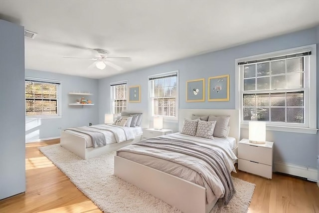 bedroom featuring baseboard heating, ceiling fan, multiple windows, and light hardwood / wood-style flooring