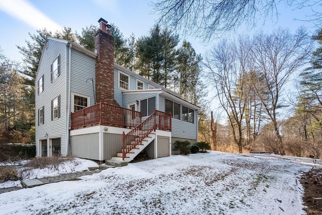 snow covered property with a garage, a wooden deck, and a sunroom