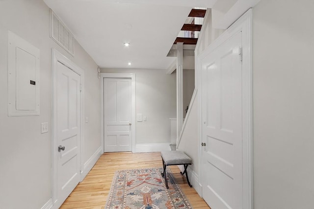 corridor featuring baseboards, visible vents, light wood finished floors, and electric panel
