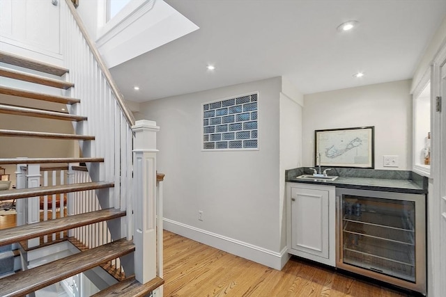 bar with stairs, beverage cooler, a sink, light wood-style flooring, and bar area