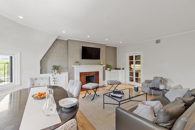 living room with crown molding, visible vents, a fireplace, light wood-style floors, and recessed lighting