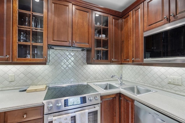 kitchen featuring appliances with stainless steel finishes, a sink, light countertops, decorative backsplash, and glass insert cabinets